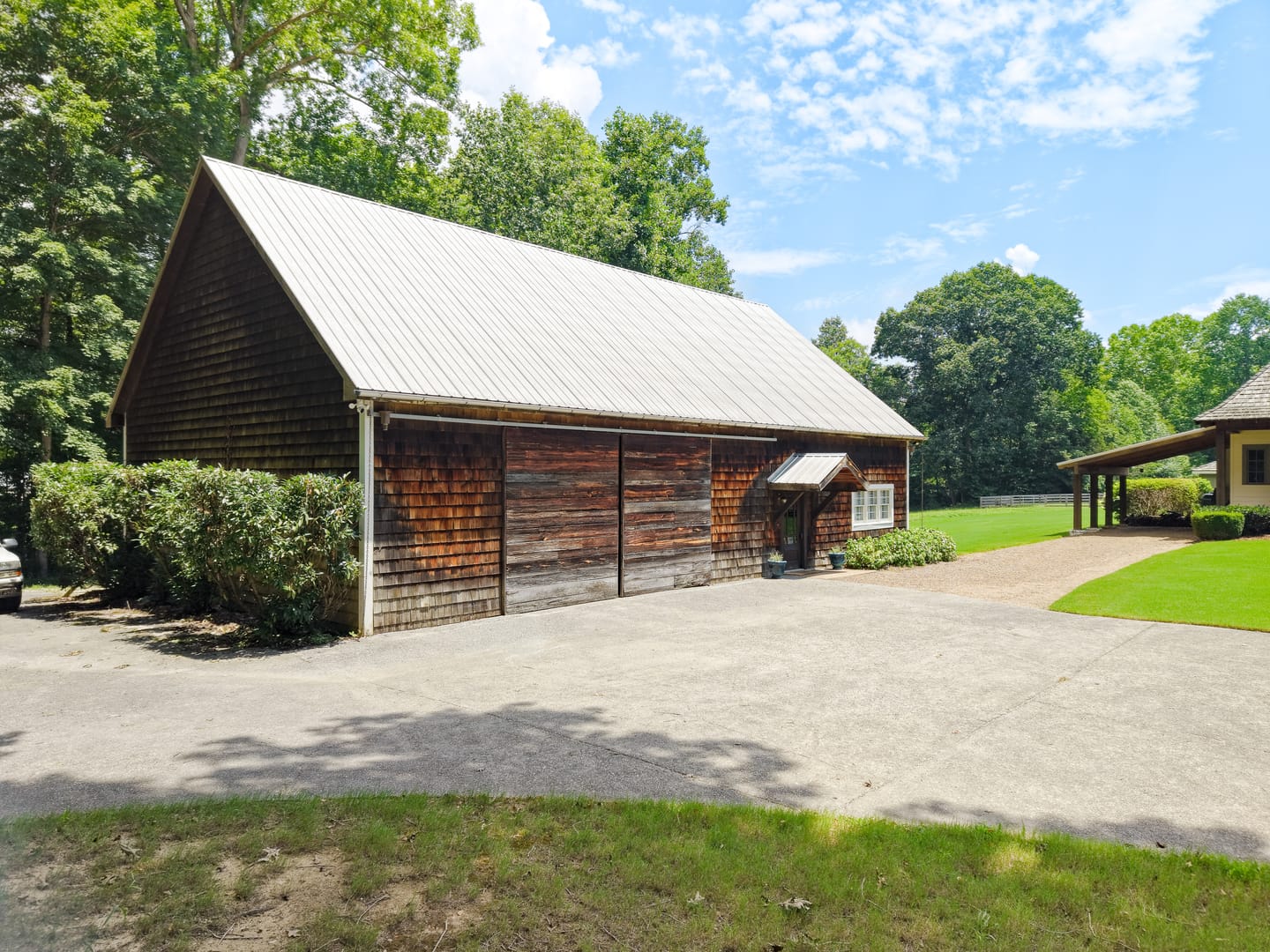 Carriage house with cedar shingle siding, a metal roof and sliding barn doors beside the drive