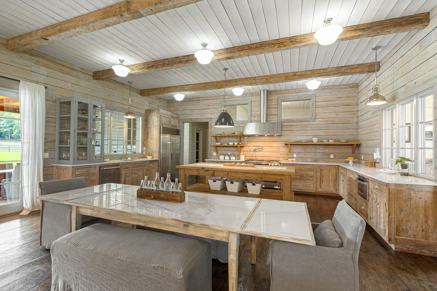 Dining table and kitchen beneath reclaimed beams