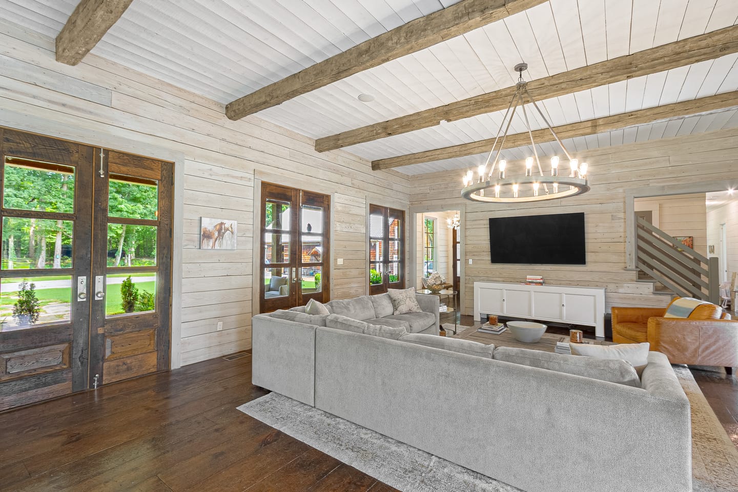 Great room under a ceiling of reclaimed hand-hewn beams, with French doors and a staircase