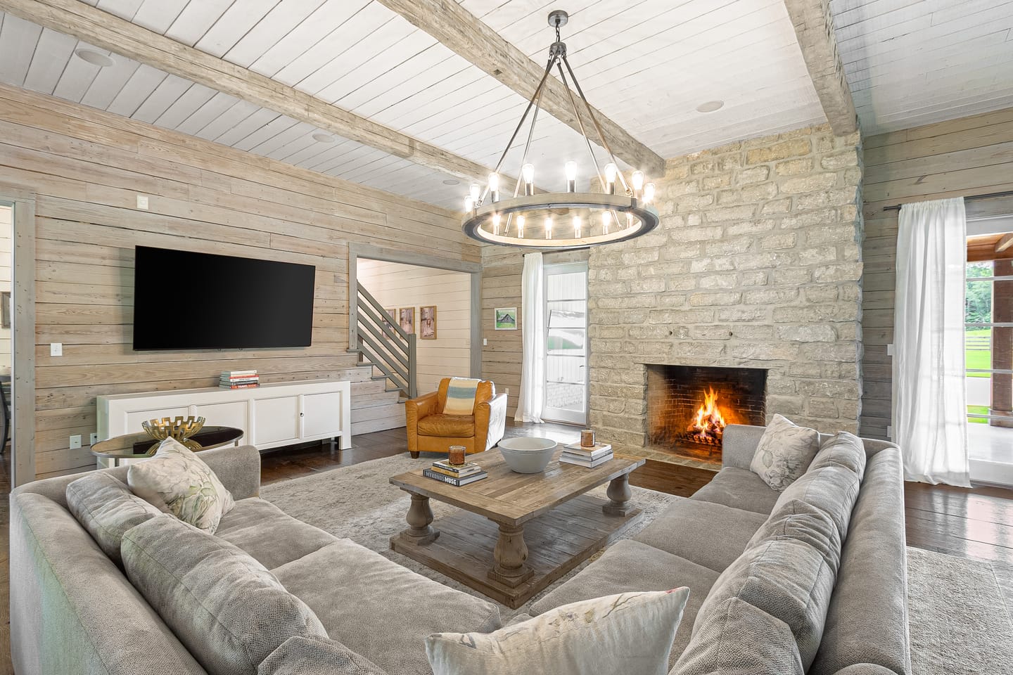Great room with a stone wood-burning fireplace, a round iron chandelier and a beamed ceiling