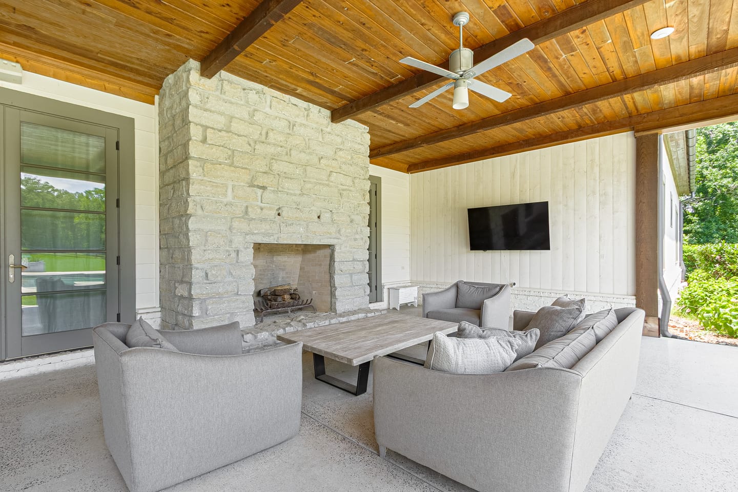 Outdoor living room seating around a stone fireplace under a wood ceiling