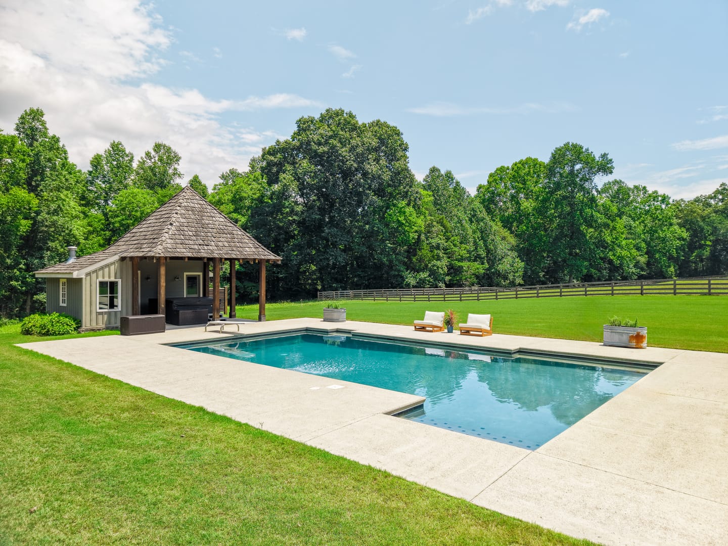 Pool and pool house with the tree line and fenced pasture beyond