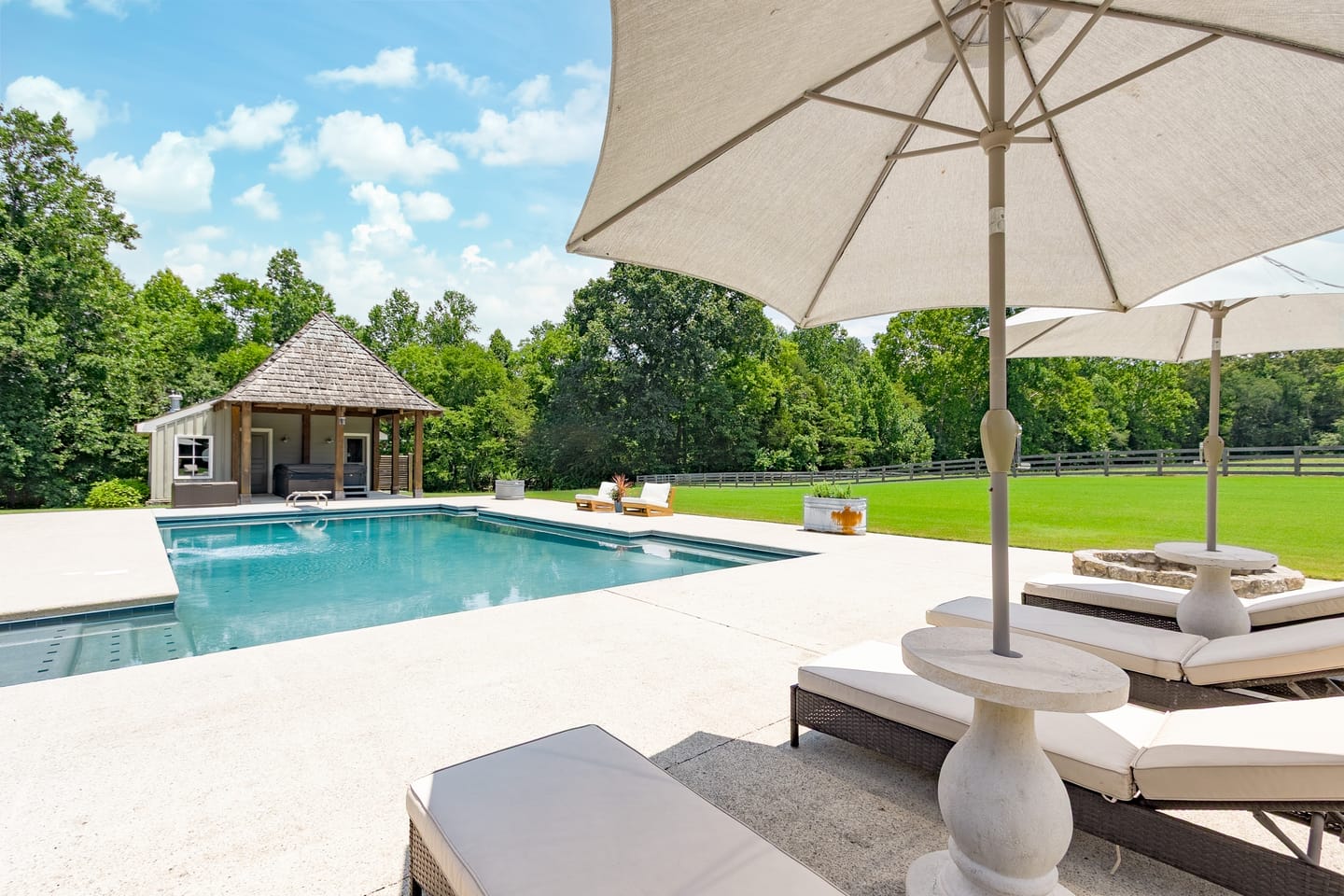 Pool deck with umbrellas and loungers, the pool house beyond