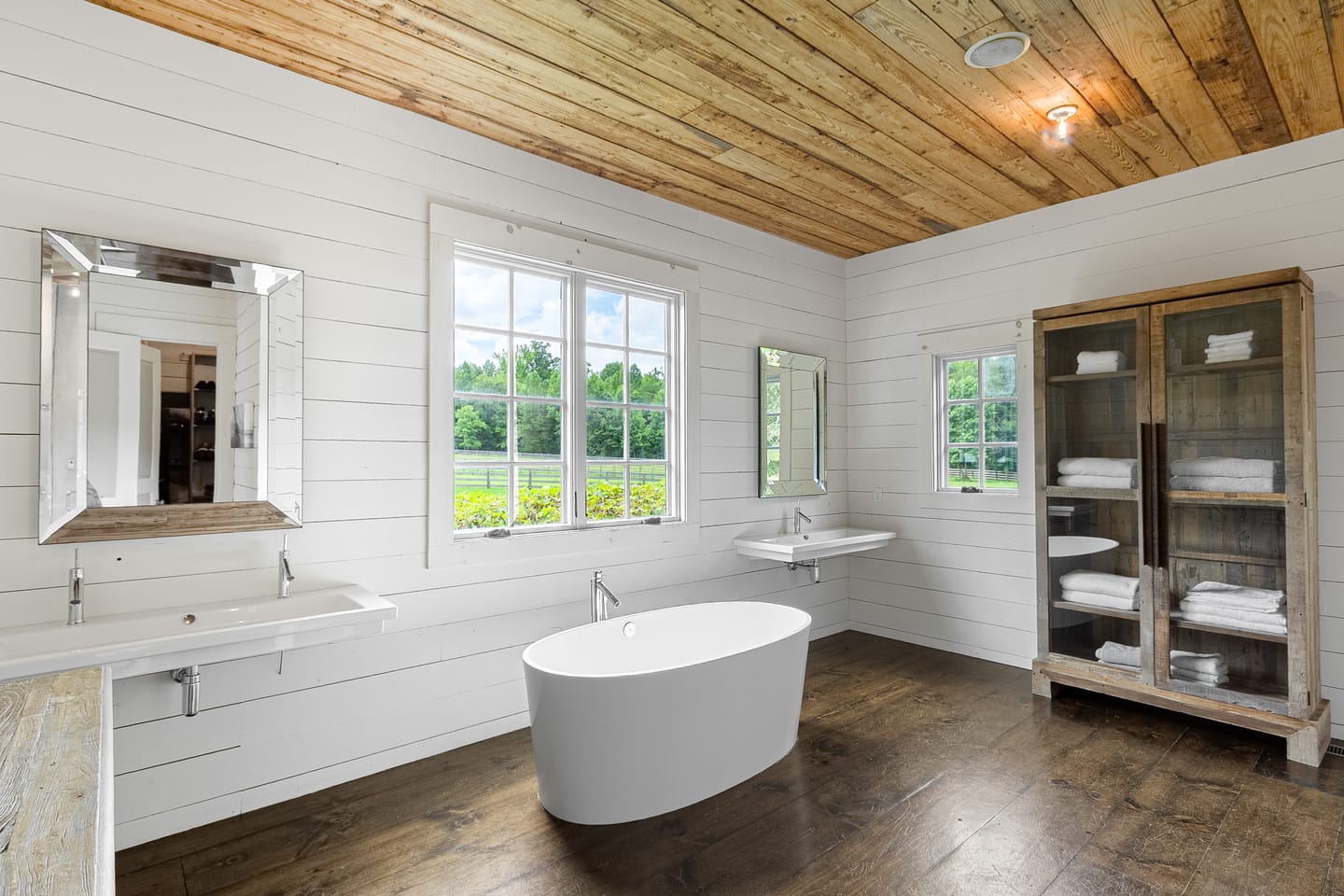 Primary bath with a freestanding tub, wall-mounted sinks and a wood plank ceiling